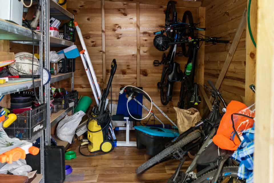 Un garage en désordre avec du matériel sportif, des vélo, du matériel de nettoyage et beaucoup de bazar