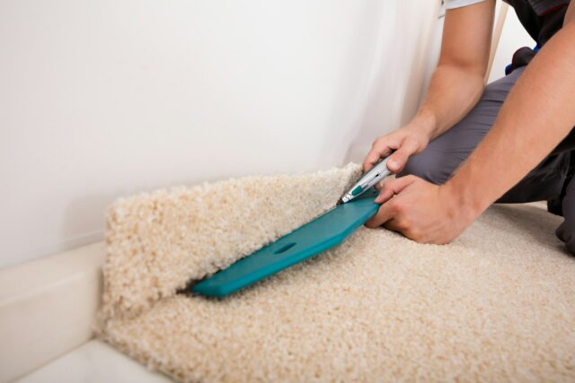 Un artisan est en train d'appliquer de la moquette au niveau d'une plinthe - Maîtrise d'œuvre et gestion de chantier à Annecy et en Haute-Savoie