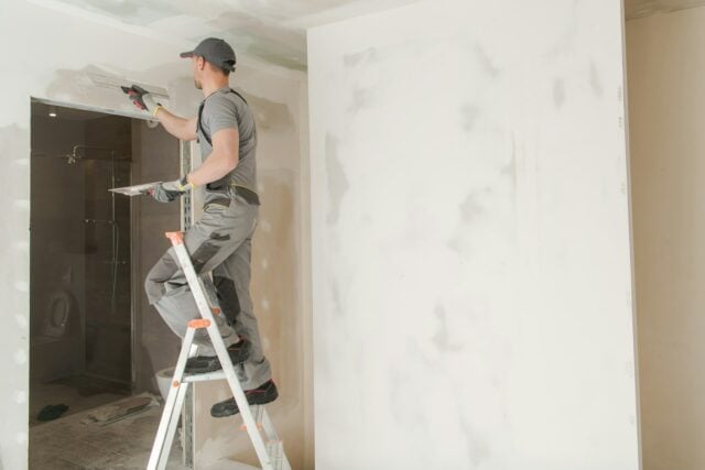 A man is standing on a ladder painting a room.