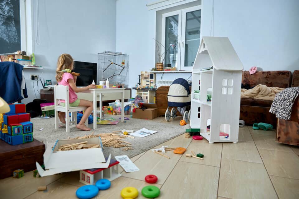 Une petite fille est assise à une table d'enfant dans une pièce de la maison, au milieu d'un désordre sans nom...