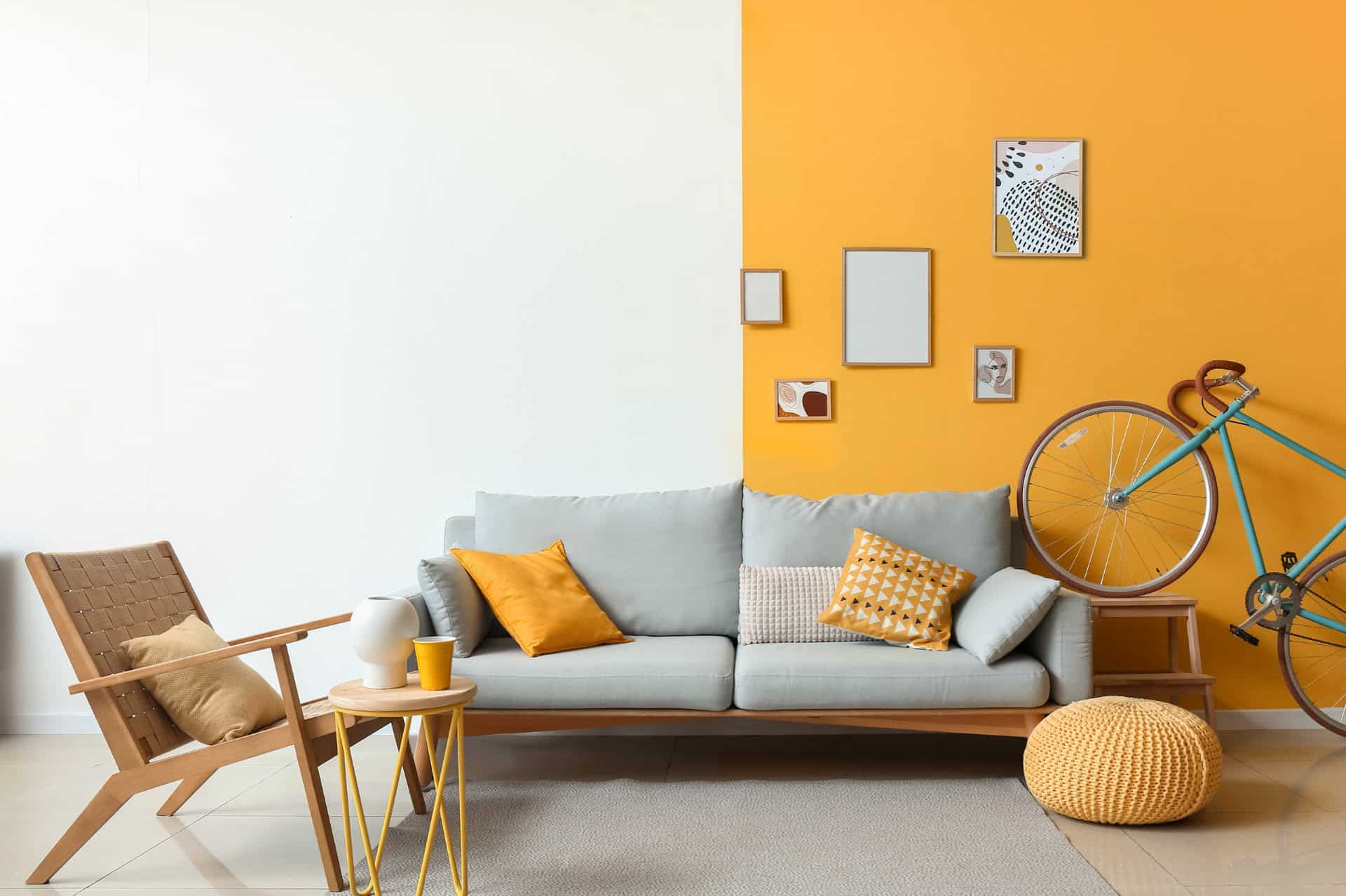 Photo d'un intérieur coloré avec un canapé, une chaise, une table d'appoint et un vélo devant un mur. Le mur est blanc à gauche et peint en jaune foncé à droite - ArchiBienPensé, architecte d'intérieur à Annecy
