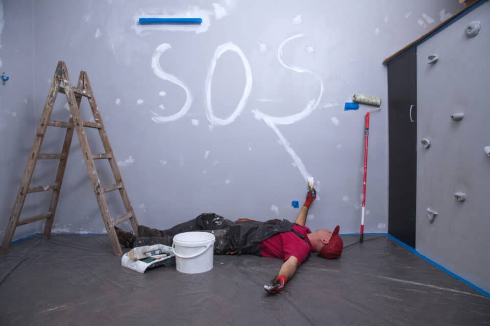 Un artisan épuisé et allongé sur le sol. Il a écrit "SOS" sur le mur avant de s'effondrer