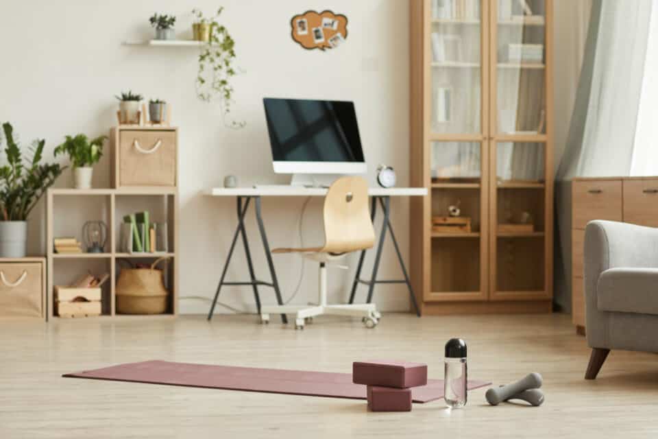Un salon servant aussi de bureau et de salle de sport. Un tapis de yoga est déroulé sur le sol à côté d'haltères et d'une bouteille d'eau